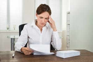 Concerned business woman sitting at desk reviewing financial statements. Bankruptcy is becoming increasingly common for licensed professionals who may be burdened by high annual professional fees and/or tuition debt.